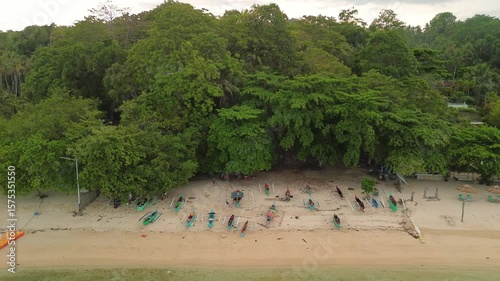 Wallpaper Mural Low aerial slide shows rows of colorful banca boats resting on soft sand beneath dense tropical trees beside Pangubatan’s calm emerald shallows on Samal Island, Philippines. Torontodigital.ca