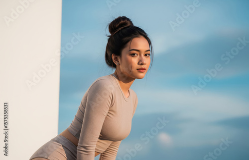 Confident young in sleek neutral tracksuit and hotpants strikes sensual pose against vast blue sky with white clouds