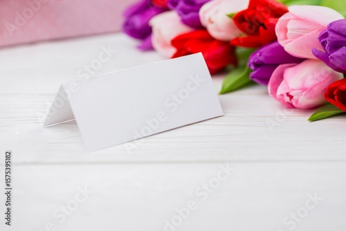Fototapeta Naklejka Na Ścianę i Meble -  Folded tent card is standing on wooden tabletop, showing flat design with tulip bouquet, copy space