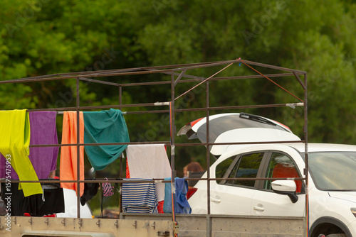 Fototapeta Naklejka Na Ścianę i Meble -  A white car is carefully parked behind a large truck that has various clothes hanging out from the back of the vehicle, creating a unique scene