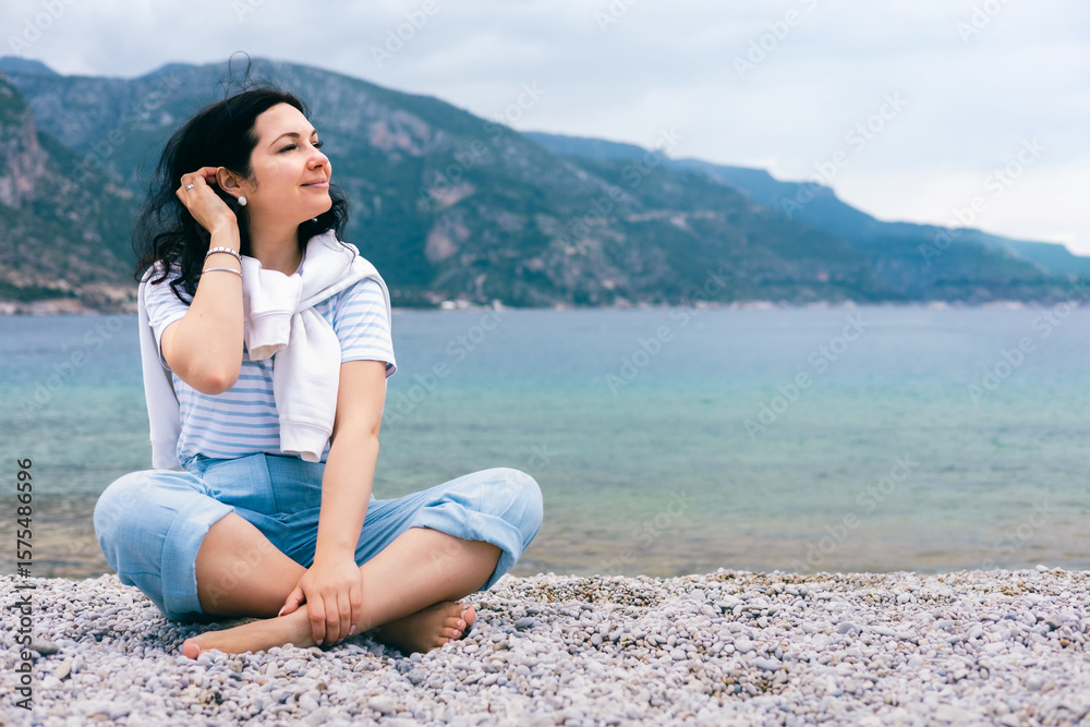 Peaceful Young Woman Sitting on Pebble Beach Enjoying Breeze and Mountain Sea View Peaceful Young Woman Sitting on Pebble Beach Enjoying Breeze and Mountain Sea View
