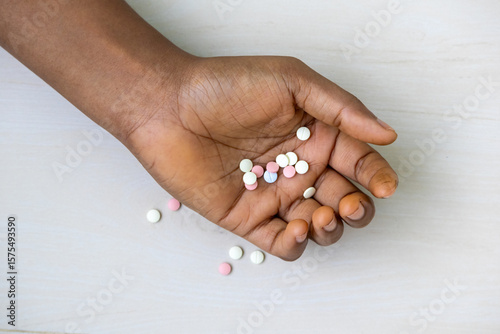 Top view of a female hand with numerous pills lying on the floor. This image represents drug addiction, medical abuse, narcotic dependence, and the risk of overdose.