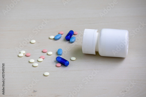 Assorted tablets, capsules, and pills scattered on the floor with a fallen medicine bottle nearby. Pharmaceutical drugs for health and illness.
