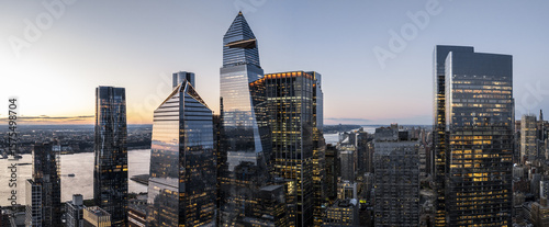 Aerial view of gleaming skyscrapers pierce the twilight sky, their glass facades reflecting the soft hues of sunset over the Hudson River, New York, New York, United States.