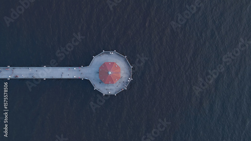 Aerial view of the Manhattan Beach Pier stretching into the dark ocean, a contrast of red and grey against the blue, Los Angeles, California, United States.