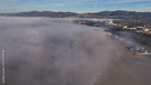 Aerial view of a thick fog blanketing the beach, with the city skyline barely visible in the distance, creating an ethereal coastal landscape, Los Angeles, California, United States.