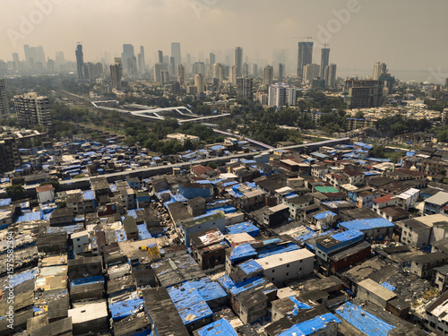 Aerial view of a stark contrast between the dense, blue-roofed shanties and the towering skyscrapers, a testament to urban disparity, Dharavi,Mumbai, Maharashtra, India.