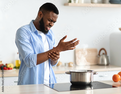 Man holding wrist in pain after touching boiling pot, kitchen accident