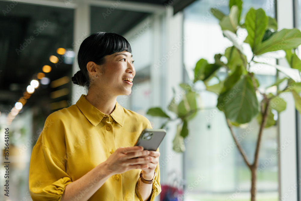 © Westend61 - Smiling woman in yellow shirt texting on phone in modern office © Westend61 - Smiling woman in yellow shirt texting on phone in modern office