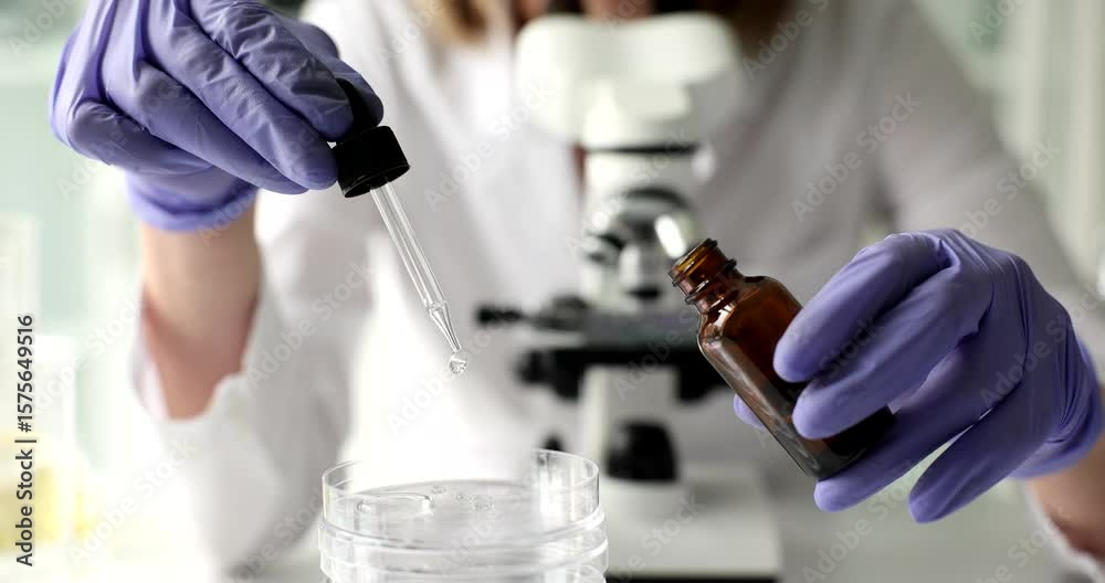 Lab assistant fills pipette drawing transparent liquid from brown vial into Petri dish. Dropper moves with precision releasing drops into clear sample