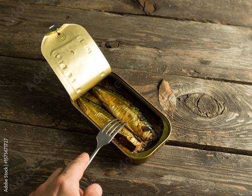 Open tin can of sardines on rustic wooden table, showcasing delicious fish ready to eat, with a fork poised to serve, highlighting culinary experience and simplicity of meal preparation