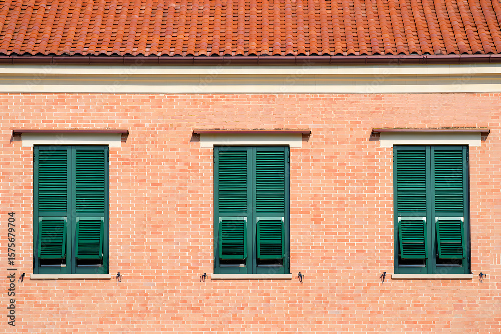 Three dark green shutters on a light brick building with a terracotta roof; sunny, Mediterranean style. Three dark green shutters on a light brick building with a terracotta roof; sunny, Mediterranean style.