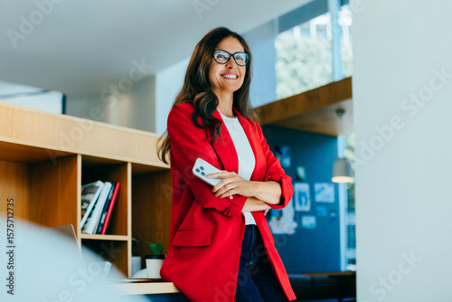 Photography Confident businesswoman in red jacket holding smartphone in bright office enviro