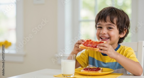 Happy young boy eating toast with jam and drinking milk at home  