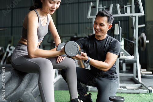 Personal Trainer Assisting Female Client with Dumbbell Exercise. Focus on Strength Training.