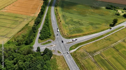 Aerial top down showing cars and travel camper trailer on suburb highway junction of American town. Sunny day with farm fields in countryside. Forest trees in summer season.