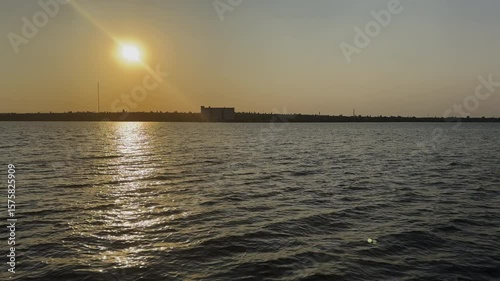 A wide expanse of water with gentle waves under an orange yellow sunset sky, with a distant shore on the horizon. Ukraine