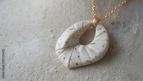 Close up of a speckled white pendant with gold chain on a textured surface in soft lighting