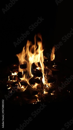 Stacked firewood ablaze in a fireplace, with glowing flames and flickering sparks creating a cozy and intense visual against a completely dark background