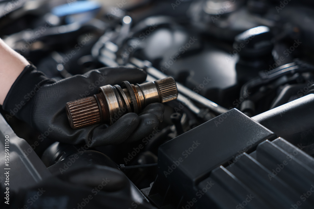 Naklejka premium Auto part. Professional mechanic with drive shaft near open hood of car indoors, closeup