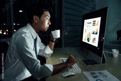 Billede på lærred Asian businessman staying up late while drinking coffee and analyzing business charts on desktop screen