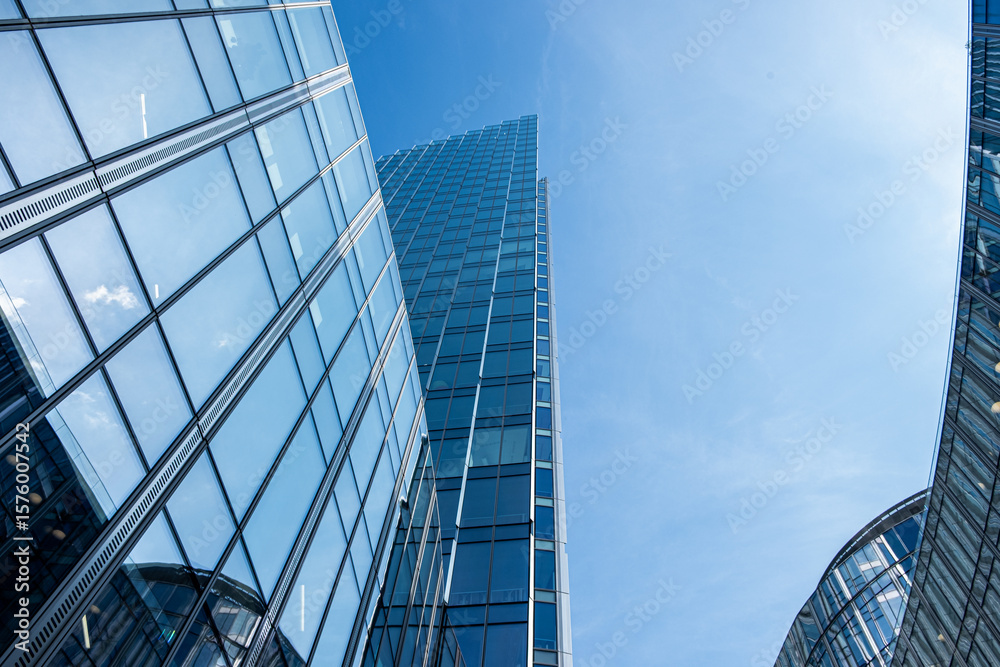 Obraz premium Modern skyscrapers with reflective glass facades rise against a clear blue sky, showcasing architectural design and urban development in a vibrant city environment