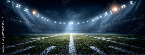 Bright stadium lights shine down on an American football field marked with white lines during a nighttime event