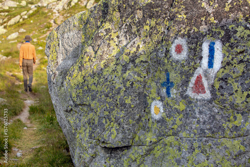 Colorful trail markers painted on lichen-covered rock in Retezat National Park. Hiker following mountain path through Romanian Carpathian wilderness.