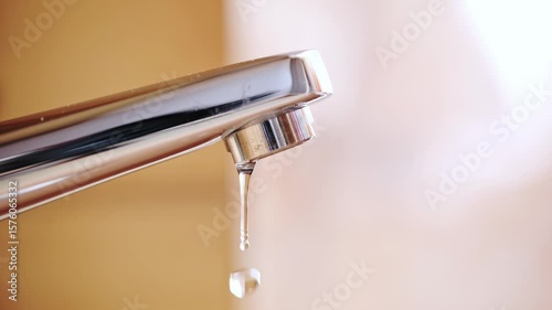 Slow motion dripping tap with water droplets inside apartment bathroom. Macro, close up, looking up shot, shallow depth of field, no people