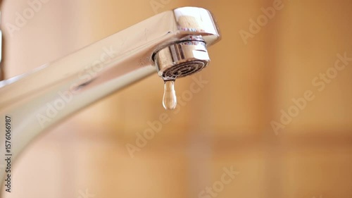 Slow motion dripping tap with water droplets inside apartment bathroom. Macro, close up, looking up shot, shallow depth of field, no people