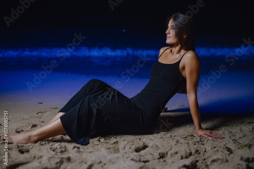 Beautiful woman sits in dress near blue sea at night 