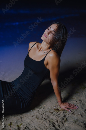 Beautiful woman sits in dress near blue sea at night 