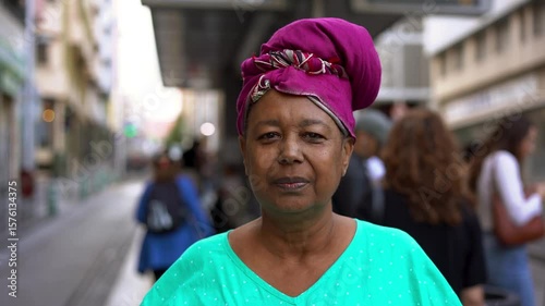 Senior african woman wearing traditional dress while looking on camera at tram station in the city - Culture and elderly lifestyle concept	