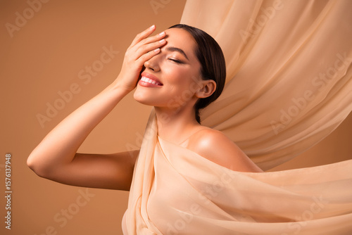 Portrait of a young woman with radiant skin and a confident smile against a beige background