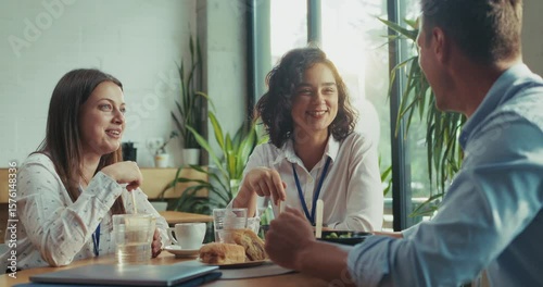 Three caucasian intern teammates enjoy lunch together in slow motion at bright sunny office cafeteria