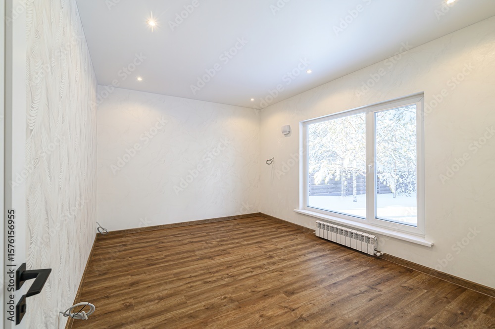 Obraz premium Bright empty room with wooden floors, white walls, and a large window showing a snowy scene