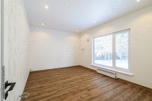 Bright empty room with wooden floors  white walls  and a large window showing a snowy scene