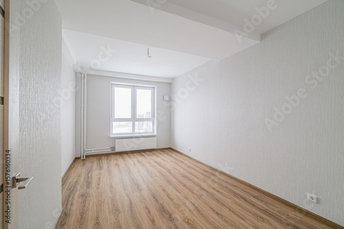 Wallpaper Mural empty, bright room with wood-like flooring. Walls are textured white/gray. A large window faces a cityscape. A partially-seen door is on the left Torontodigital.ca