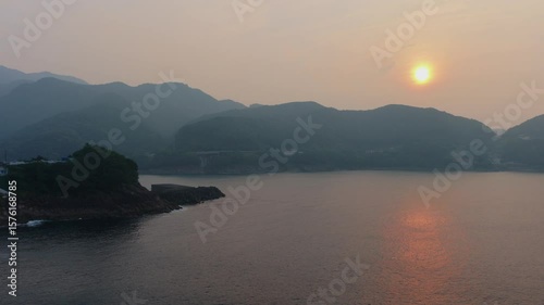 Sunrise reflection on coastal bay on hazy morning with distant mountains, aerial view