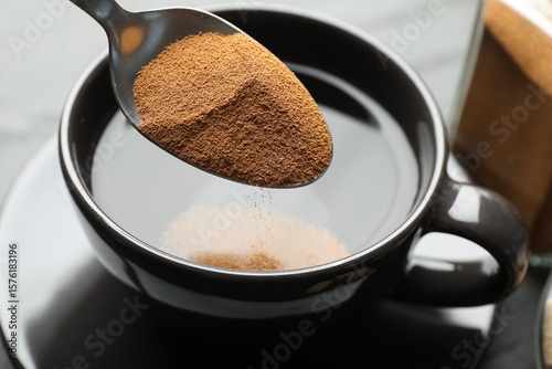 Photos Putting instant coffee into cup at table, closeup