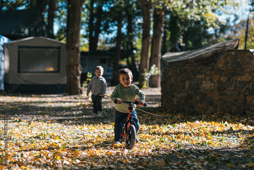 Fototapeta premium Children riding balance bikes at campground in autumn forest