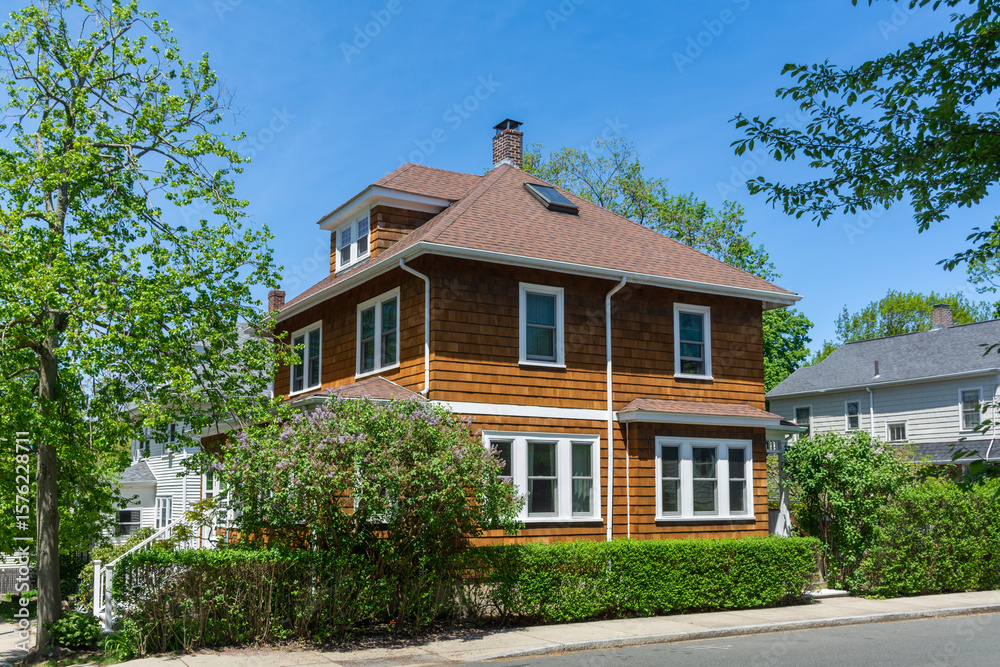 Beautiful two-story classic American house with natural brown siding and lush green hedges in Brighton, Massachusetts, USA Beautiful two-story classic American house with natural brown siding and lush green hedges in Brighton, Massachusetts, USA