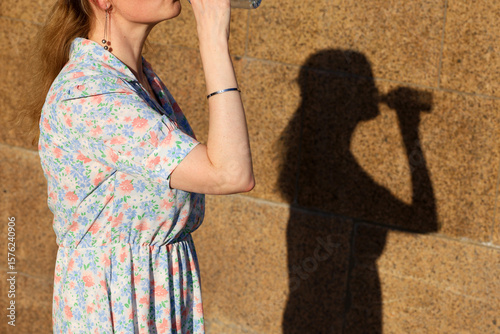 Woman drink water from the bottle on a street, shadow on stone wall. Concept of thirst, hot weather in summer city