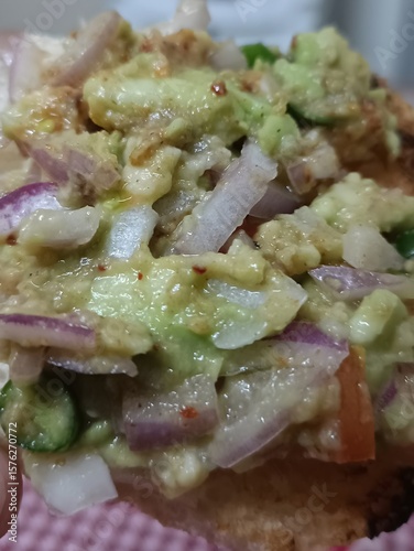 Close-up of a spicy Indian-style avocado and onion chaat served on crispy toast. A flavorful snack or appetizer with creamy texture and vibrant ingredients.