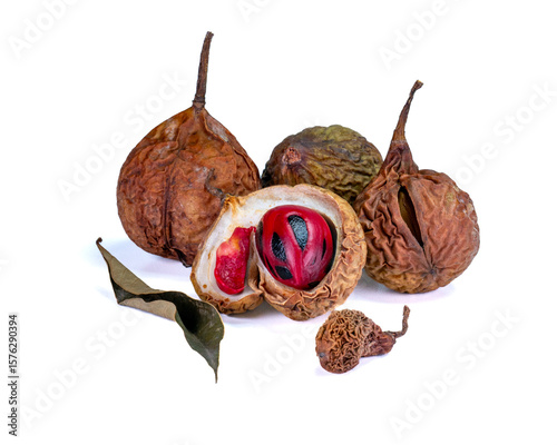 Several dried nutmegs with one open revealing the nutmeg seed and bright red mace, with dried leaves as decoration, isolated on a white background