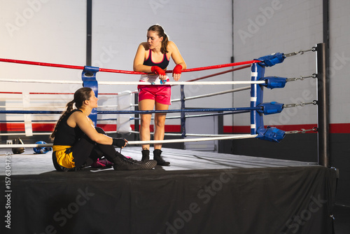 Female sparring partners resting in boxing ring leaning on ropes while holding gloves, copy space