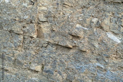Texture, background layers and cracks in sedimentary rock on cliff face. Cliff of rock mountain. Wild stone protruding crumbling layered blocks.