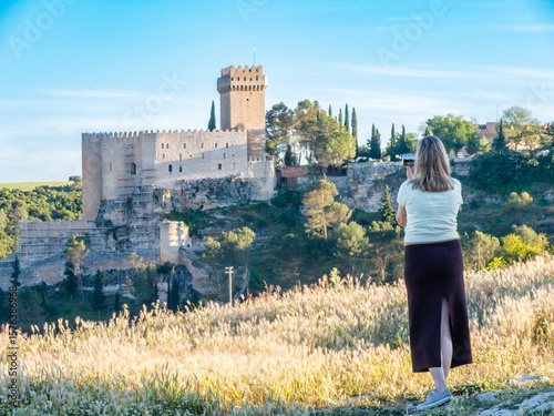 Young woman taking photos with her cell phone of the town of Alarcón with the Jucar River and the walled enclosure of the castle, declared a historic-artistic site.