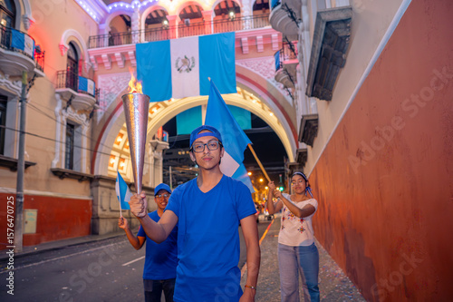 Portrait of young Guatemalans in front of a neoclassical building. They hold flags and a flaming torch.