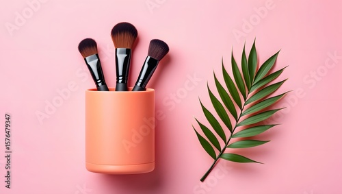 Makeup brushes in container with palm leaf on pink background beauty product concept